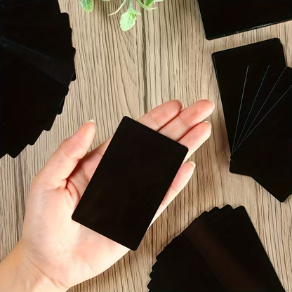 Hand holding a black square business card sample on a wooden surface with more card samples scattered around.