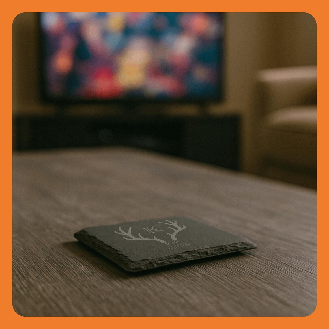 A decorative coaster with a deer antler design on a wooden table, with a blurred TV in the background.