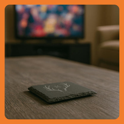 A decorative coaster with a deer antler design on a wooden table, with a blurred TV in the background.