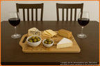 A cheese platter with various cheeses and olives, accompanied by two glasses of red wine on a wooden table.