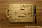 Wooden cutting board with engraved text 'The Anderson Home' and decorative vines, accompanied by a knife.